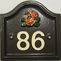 This is a Lancaster Plus number plaque showing ivory numerals on a brown background and a small orange-peach rose cluster